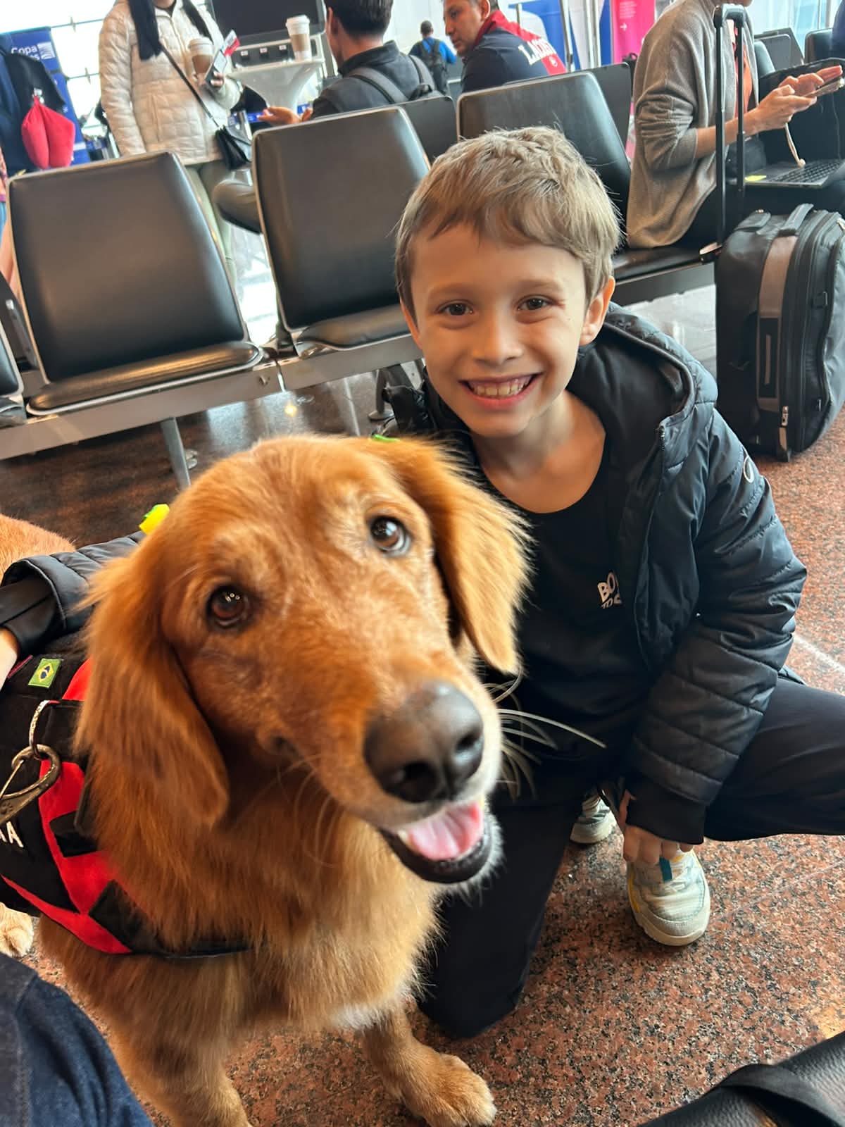 Menino sorrindo com seu cão de serviço no aeroporto antes do voo internacional